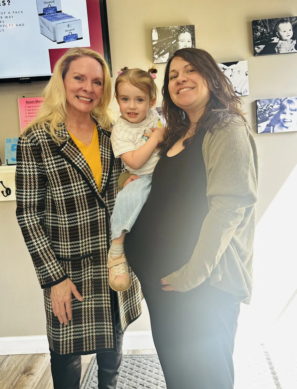 Dr. Anna Saylor smiling beside a mom-to-be who holds her toddler in our reception area