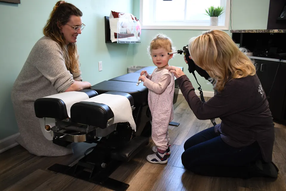 Dr. Anna Saylor gently checking a toddler who stands on the adjusting table beside a team member