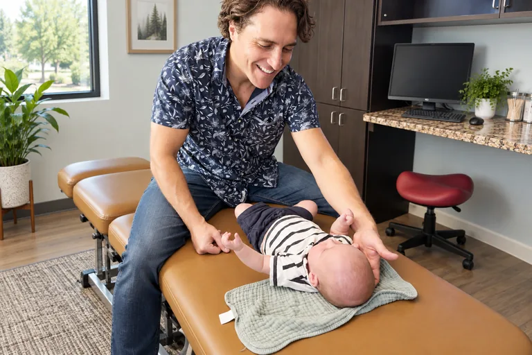 Dr. Zach Conner smiling as he gives a baby a gentle adjustment